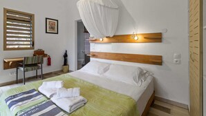 Ein ordentlich eingerichtetes Schlafzimmer mit Bett, Nachttisch, Sessel, einem Fenster mit Jalousien und einer Wandleuchte.