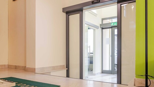 Eine Hotelhalle mit grünem Teppich, einem Empfangstresen und einer Glastür zu einem weiteren Bereich.