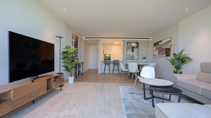Un salon moderne doté d’un téléviseur à écran plat, d’un meuble de rangement en bois, d’une plante en pot, d’un coin repas avec des chaises et d’un canapé.