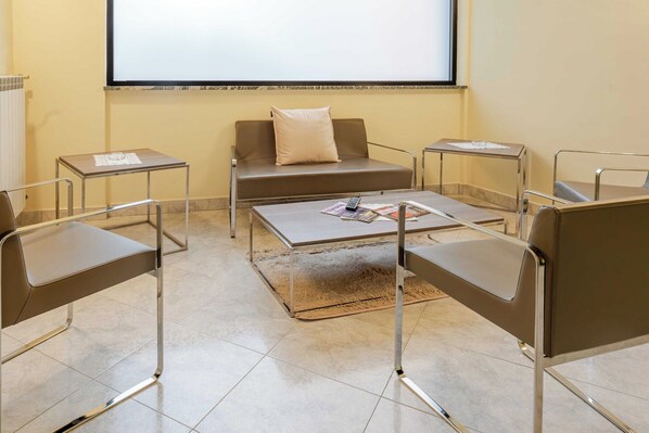 A conference room with a sofa, two armchairs, a coffee table, and a projector screen.
