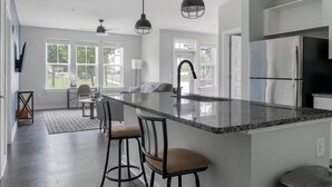 A modern kitchen with a large island, bar stools, and a refrigerator.