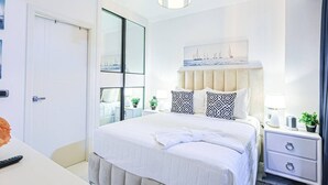 Una habitación de hotel moderna con una cama grande, mesitas de noche, un cabecero con un detalle decorativo y un ventanal amplio.