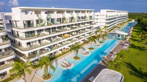 Un hotel de varios pisos con una gran piscina, mobiliario exterior y palmeras.