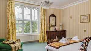 A hotel room with a large window, a chandelier, a wooden dresser, and a bed with towels.