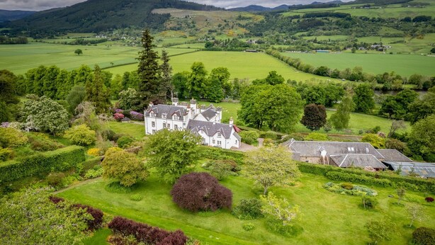 A large estate with a main house and several outbuildings, surrounded by lush green fields and trees.