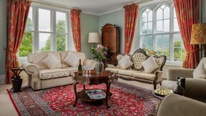 A traditional sitting room with two sofas, a coffee table, and a large window with curtains.
