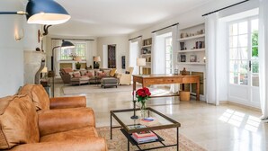 A spacious living room with a leather sofa, a coffee table, and a wooden desk. There are bookshelves and a fireplace in the background. - Bastide Blanche - Five Bedroom Villa, Sleeps 12 (Vence)