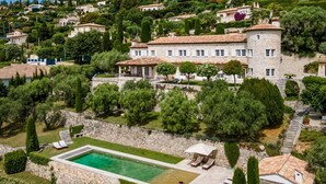 A large stone building with a swimming pool, surrounded by lush greenery and other houses. - Bastide Blanche - Five Bedroom Villa, Sleeps 12 (Vence)