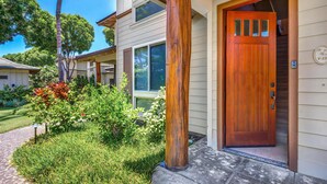 Una casa con puerta de madera, un porche pequeño y un jardín bien cuidado con diversas plantas y un camino.
