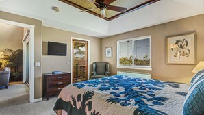 Un dormitorio con cama, una silla, televisor, ventilador de techo y ventana con persianas.