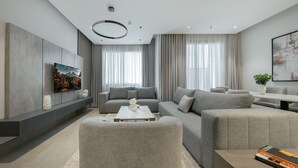 Ein modernes Wohnzimmer mit einer grauen Sofagarnitur, einem Couchtisch und einem an der Wand befestigten Flachbildfernseher.