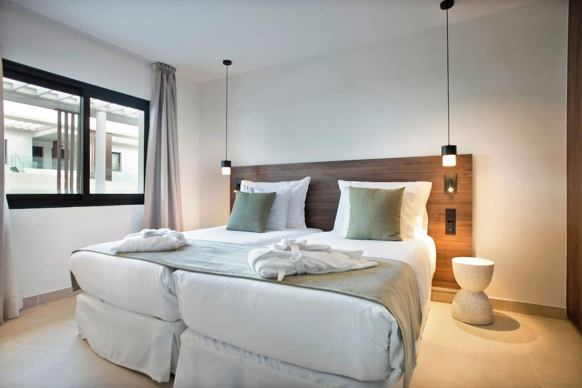 Ett modernt hotellrum med en stor säng, ett träbeklätt sänggavell och utsikt över byggnadens interiör genom ett stort fönster.