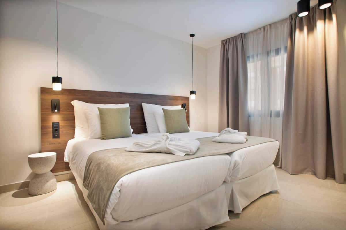 Ett hotellrum med en stor säng, två sängbord, en väggmonterad lampa och ett fönster med gardiner.