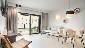 A modern hotel room with a sofa, dining table, chairs, a TV, and a sliding glass door to an outdoor area. - Coral Cotillo Reef (La Oliva)