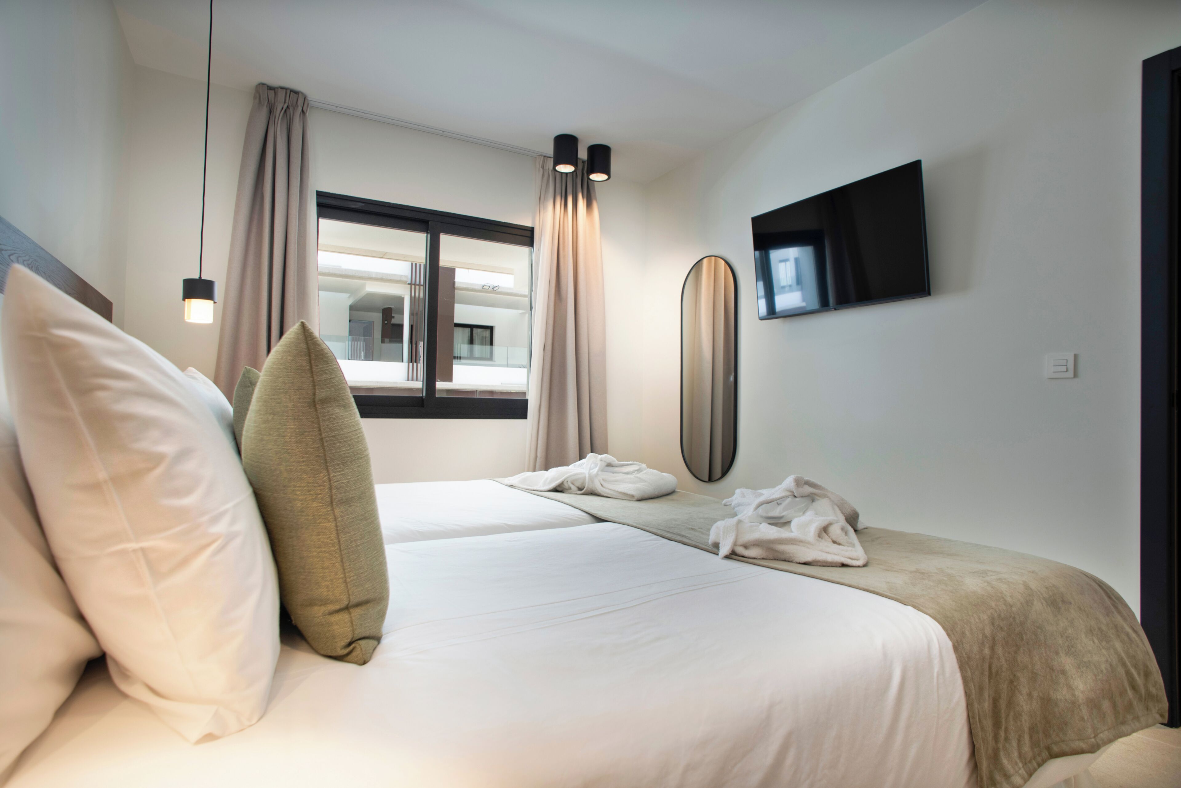 A hotel room with two beds, a large mirror, a flat-screen TV, and a window with curtains.