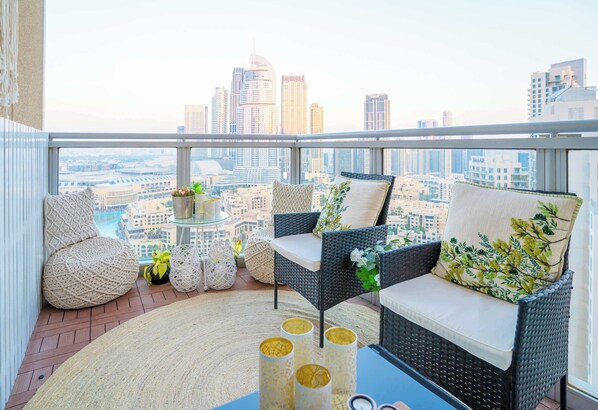 A balcony with wicker furniture, a round rug, and a view of a cityscape.