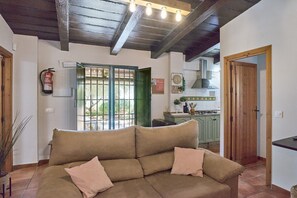 A living room with a sofa, a wooden door, a kitchen in the background, and a fire extinguisher on the wall.