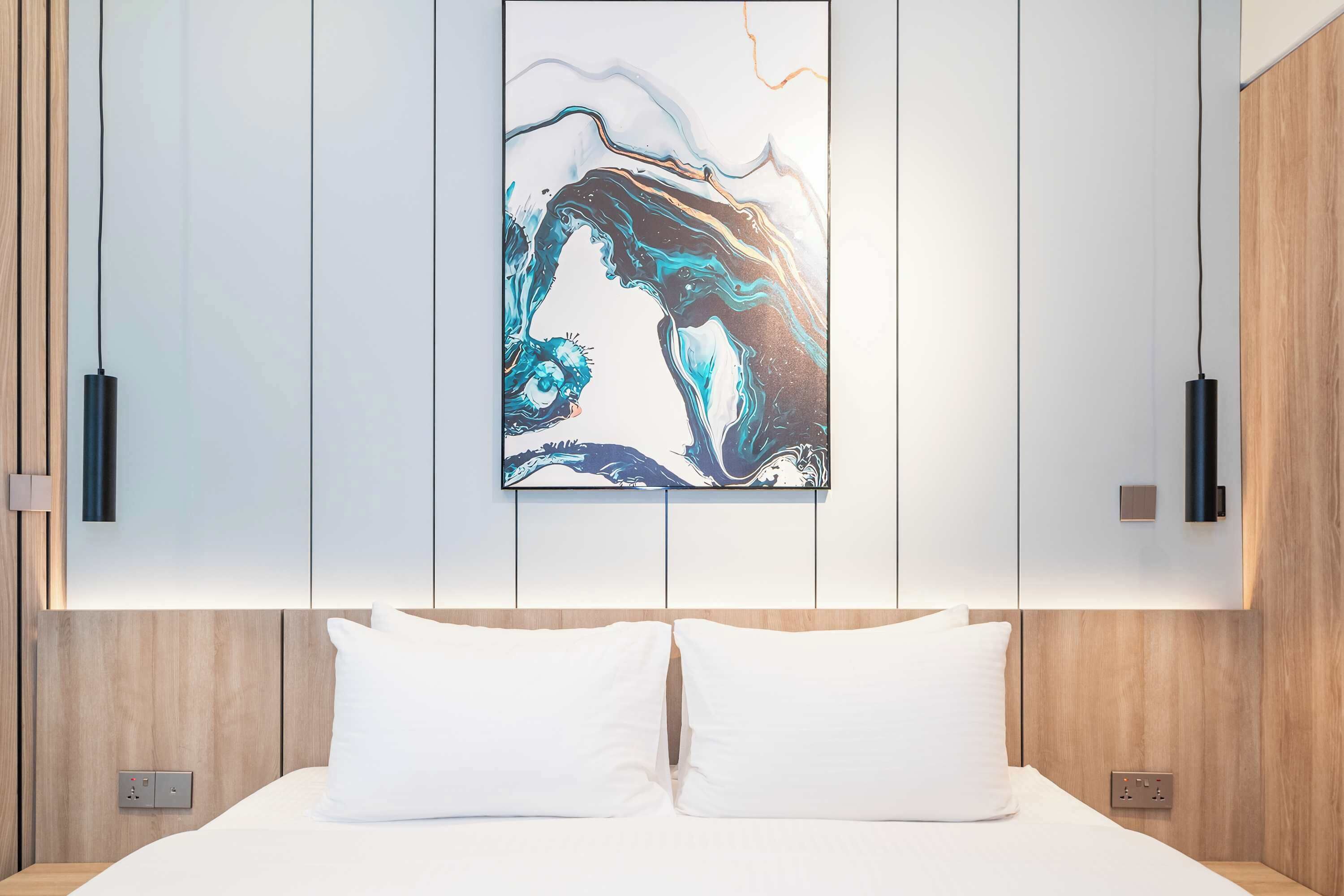 A modern bedroom with a large abstract painting on the wall, a wooden headboard, and a white bed with two pillows.
