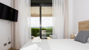 Une chambre d’hôtel moderne dotée d’un grand lit, d’un téléviseur à écran plat fixé au mur, d’un balcon avec une chaise et d’une vue sur la campagne.