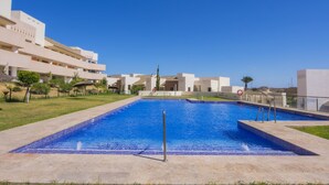 Une piscine à l’eau d’un bleu limpide, entourée d’une terrasse en béton et d’une zone herbeuse.