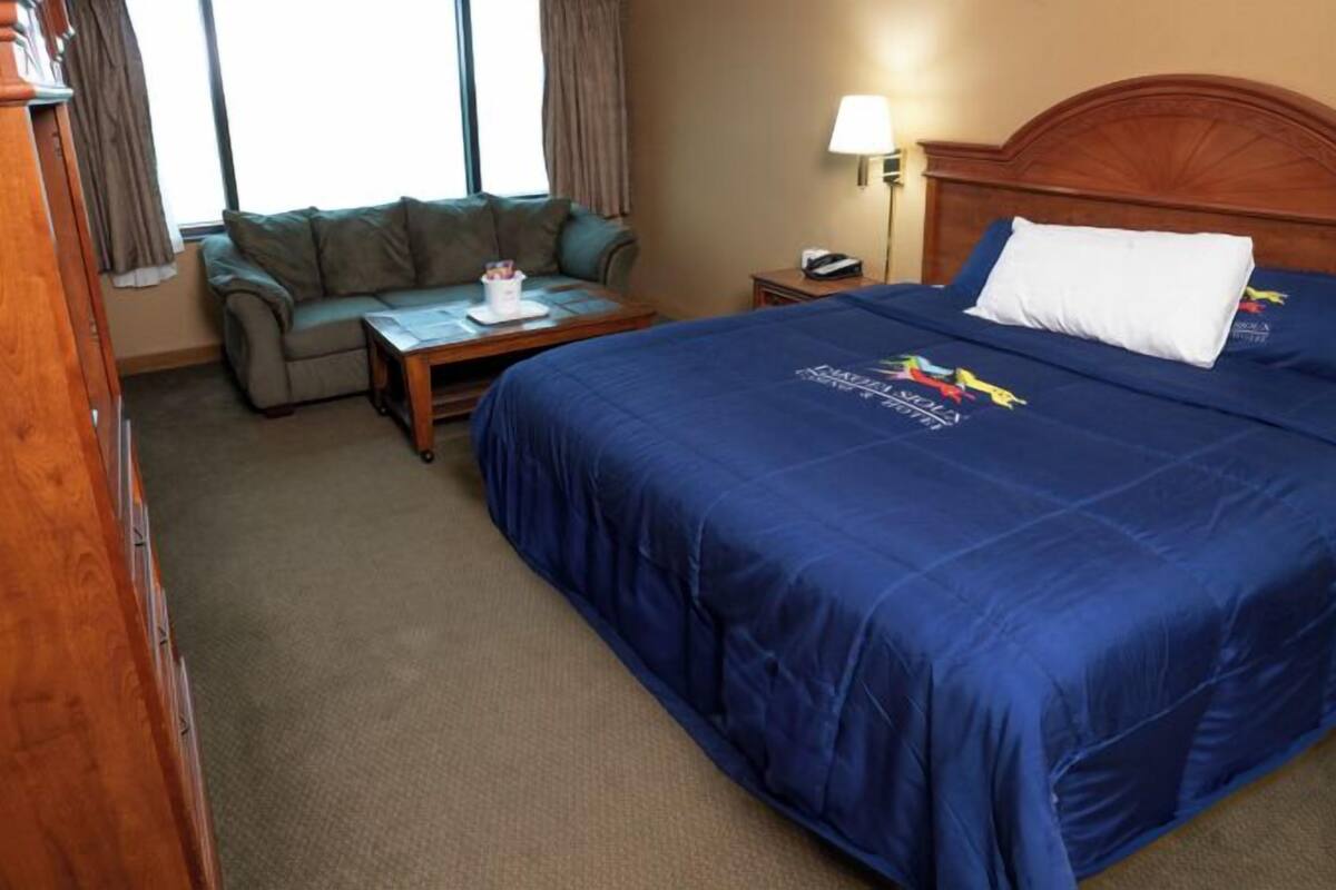 Et hotelværelse med en stor seng, et træhovedgærde, et natbord, et skrivebord og en grøn sofa.