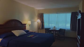 A hotel room with a bed, a desk, a chair, a lamp, and a window with curtains.