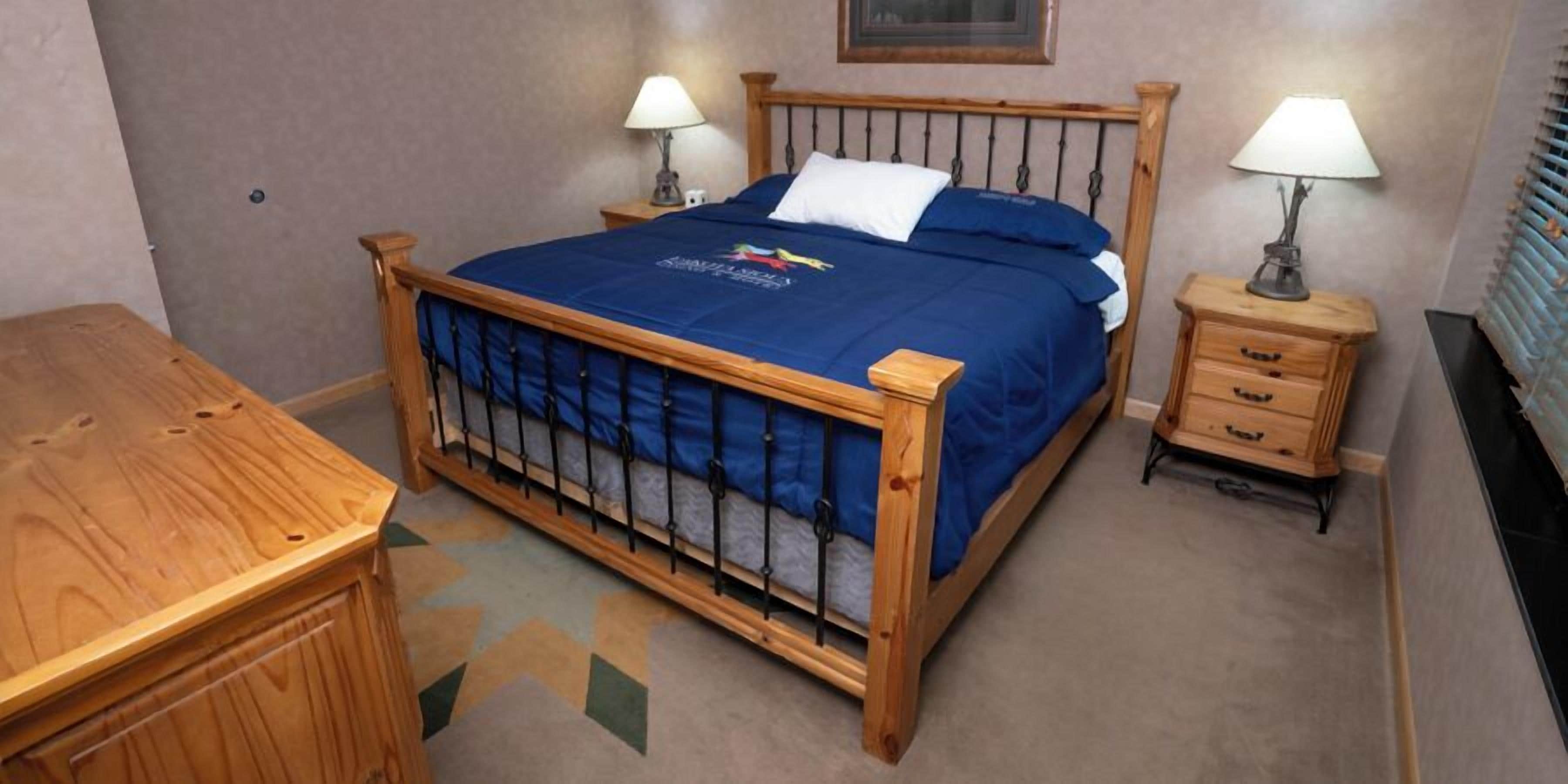 A single bed with a wooden frame, a blue bedspread, two bedside tables with lamps, and a small wooden dresser.