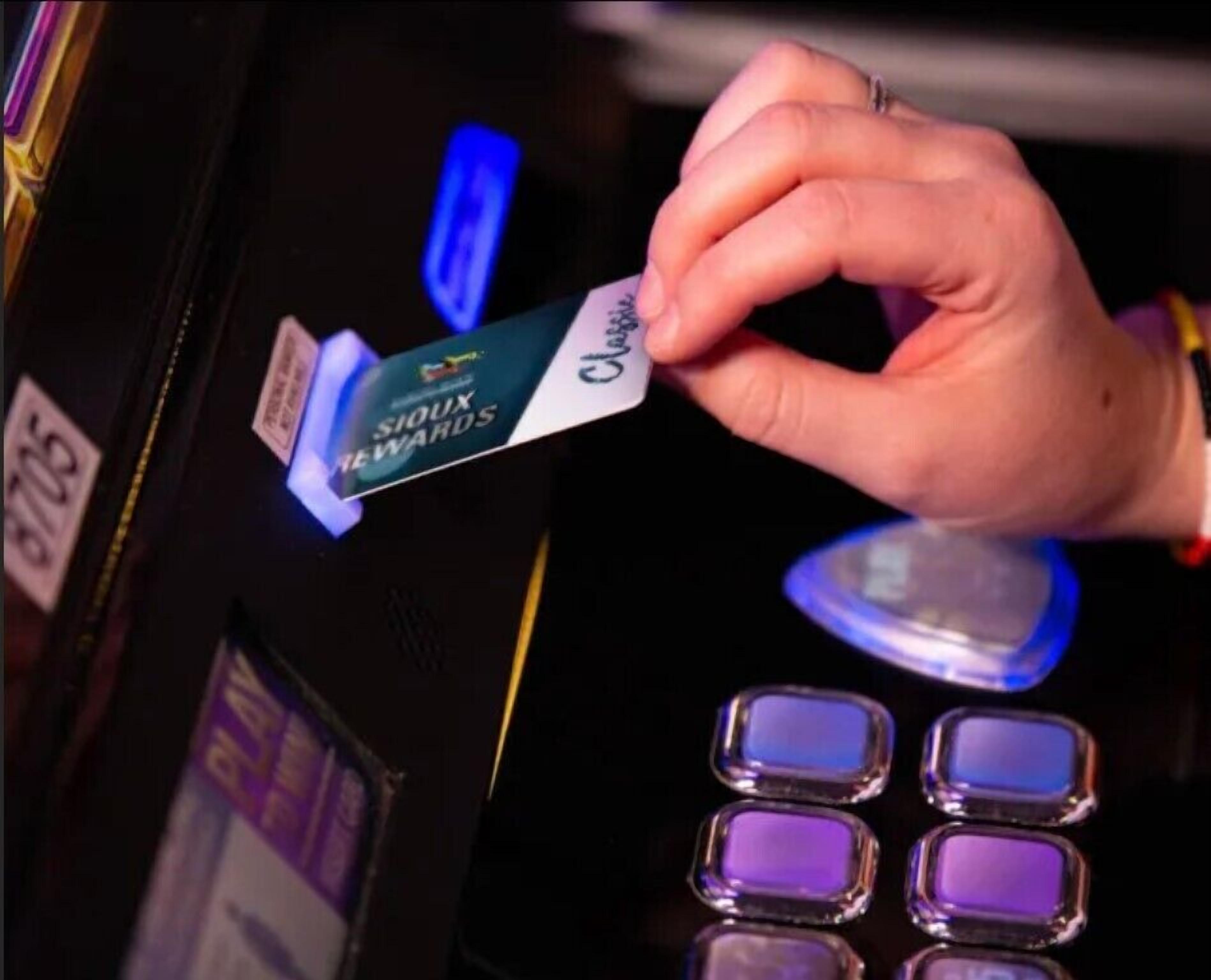 A hand holding a card labeled "SIOUX REWARDS" at a slot machine.