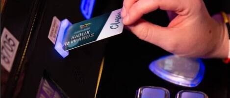 A hand holding a card labeled "SIOUX REWARDS" at a slot machine.