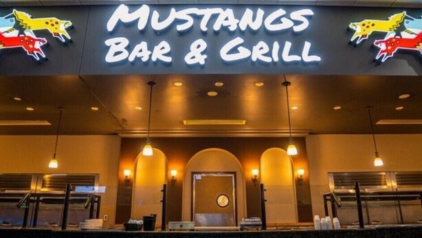 El exterior de Mustangs Bar & Grill, con un letrero de neón y adornos de caballos.