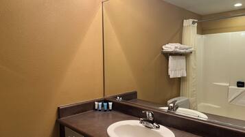 Une salle de bain avec un mur beige, un plan de toilette marron, un lavabo blanc et un miroir qui reflète l’espace de la douche.