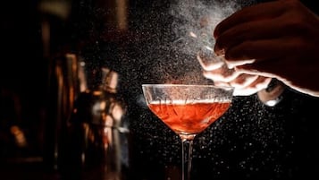 A hand sprinkling a powdery substance into a cocktail glass.