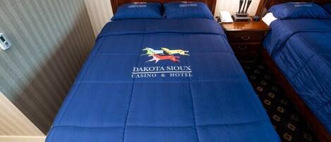A hotel room with a bed featuring a blue bedspread with the logo "Dakota Sioux Casino & Hotel" and a decorative emblem.