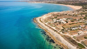 Vista aèria d'una població costanera amb una platja, aigües blaves cristal·lines i una combinació d'edificis residencials i comercials.