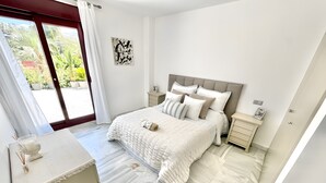 Ein Schlafzimmer mit Bett, Nachttischen, einem Schminktisch und einem Fenster mit Blick auf Grünfläche.