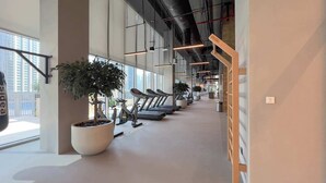 Een moderne sportschool met loopbanden, grote potplanten en grote ramen met uitzicht op de stad.