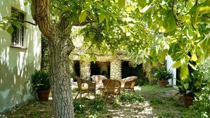 A courtyard with a tree, wicker chairs, and stone walls. - GuestHost - Relax in the natural park/20 minutes from the sea (Sassari)
