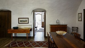 A dining area with a wooden table, chairs, a radiator, and a framed picture on the wall. - GuestHost - Relax in the natural park/20 minutes from the sea (Sassari)
