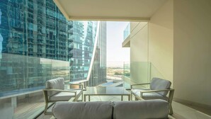 A modern balcony with a glass railing, offering a view of a cityscape and a tall building.