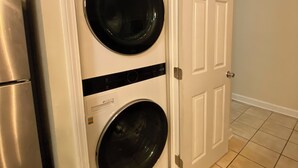 A laundry room with two stacked front-loading washing machines, a stainless steel refrigerator, and a white door with a silver handle.