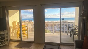 A room with a view of the beach, a sliding glass door, a chair, a table, and a sofa.