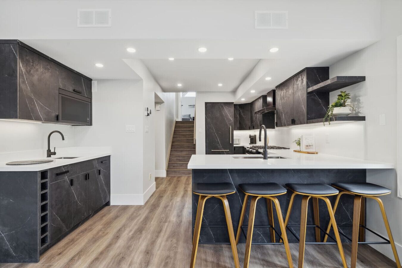 A modern kitchen with dark marble cabinets, a white countertop, and a central island with bar stools.