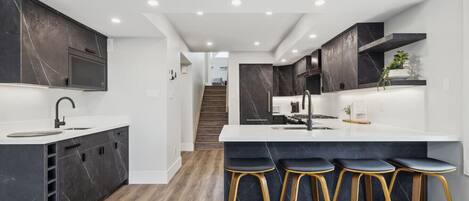 A modern kitchen with dark marble cabinets, a white countertop, and a central island with bar stools.