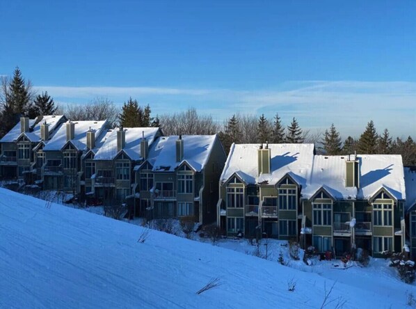 A row of multi-story buildings with snow-covered roofs, likely a hotel or resort, set against a clear blue sky.