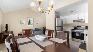 A dining area with a wooden table, chairs, a chandelier, and a kitchen in the background. - NEW Corp/Bus Townhome New Hudson (New Hudson)
