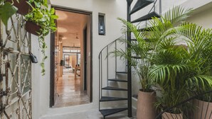 Un escalier en colimaçon menant à l’étage supérieur, entouré de plantes en pot et d’une grille en métal rustique.