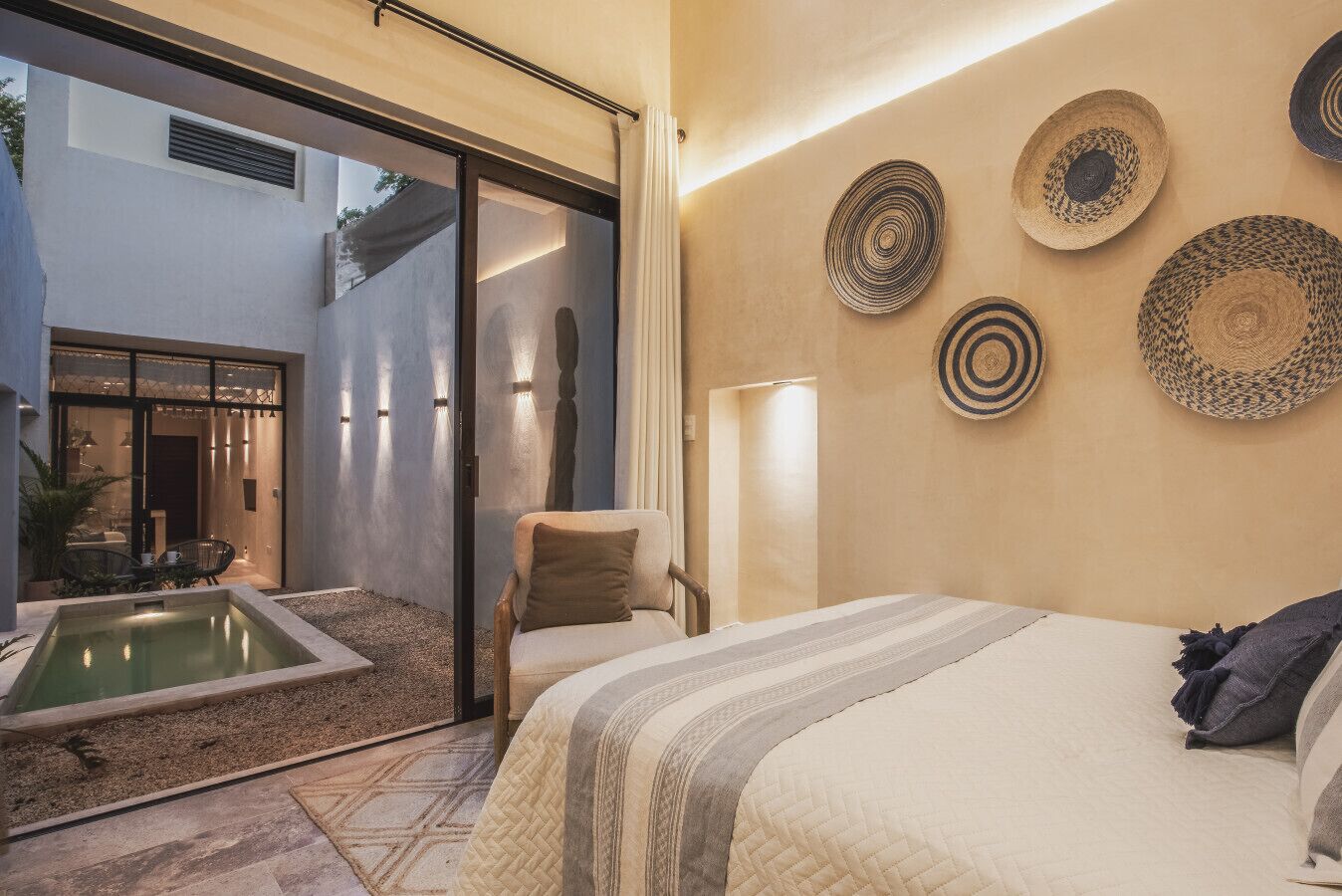 A modern bedroom with a large bed, a small seating area, a hot tub, and a view of the outside.