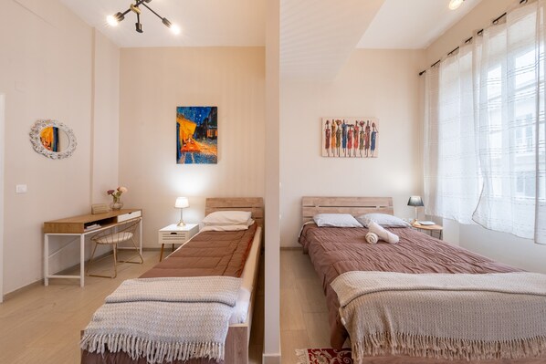 Une chambre moderne avec deux lits, un bureau, une chaise et des œuvres d’art accrochées aux murs.