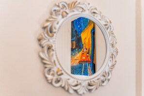 Un miroir doté d’un cadre orné, dans lequel se reflète une peinture colorée représentant une scène de rue.