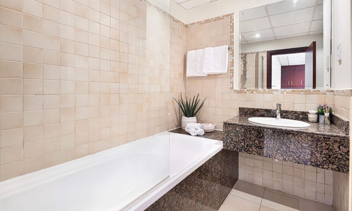 Une salle de bain moderne avec une grande baignoire, un lavabo surmonté d’un plan de travail en granit et un miroir au-dessus du lavabo.